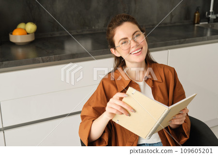 Close up portrait of beautiful young woman holding notebook, reading planner, sitting at home and studying, revising or doing homework 109605201