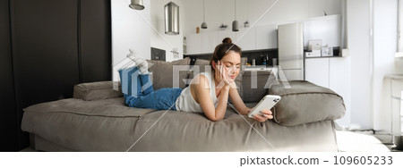 Portrait of smiling, happy young woman resting at home, resting on couch with smartphone, using mobile phone application Portrait of smiling, happy young woman resting at home, resting on couch with smartphone, using mobile phone application 109605233