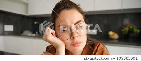 Close up portrait of woman in glasses with concerned, sad face, looking upset, troubled expression, sitting at home Close up portrait of woman in glasses with concerned, sad face, looking upset, troubled expression, sitting at home 109605301