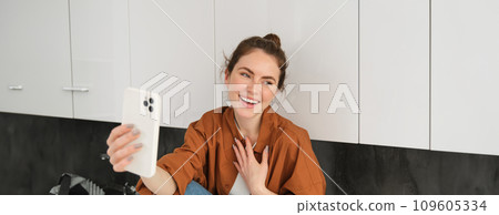 Carefree woman talking online, holding smartphone while video chatting with friend, laughing and smiling Carefree woman talking online, holding smartphone while video chatting with friend, laughing and smiling 109605334