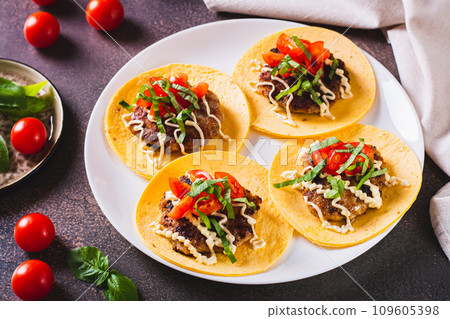 Smash Burger Tacos  with sauce, tomatoes and basil on a plate on the table 109605398