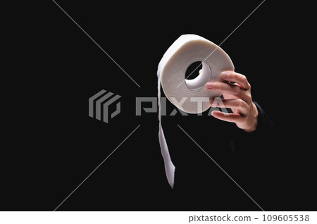 Close-up of a woman's hand using toilet paper, against a dark background. A hand holds a roll of paper. White roll of toilet paper in a woman's hand 109605538