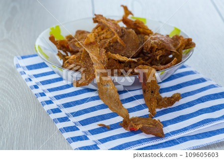dried meat with spices in a glass bowl, light wooden background. 109605603