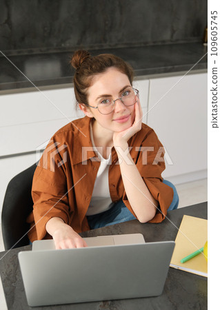 Vertical shot of woman working from home, business owner using laptop, browsing social media on computer, wearing glasses 109605745