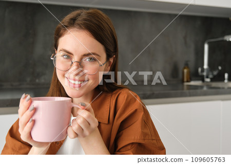 Close up portrait of cute smiling woman, spends time at home, sits in kitchen with cup of coffee, drinks tea, relaxes Close up portrait of cute smiling woman, spends time at home, sits in kitchen with cup of coffee, drinks tea, relaxes 109605763