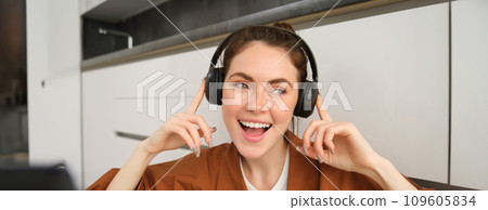 Carefree female model in wireless headphones, listens to music, enjoys favourite tunes in earphones, sings along and smiles 109605834