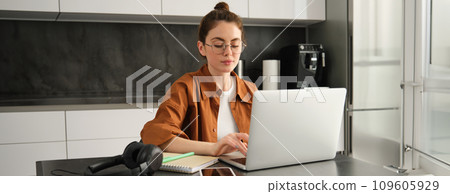 Work and life balance concept. Young woman in glasses, working from home, typing on laptop, student doing homework on computer, sitting in kitchen, freelancing 109605929