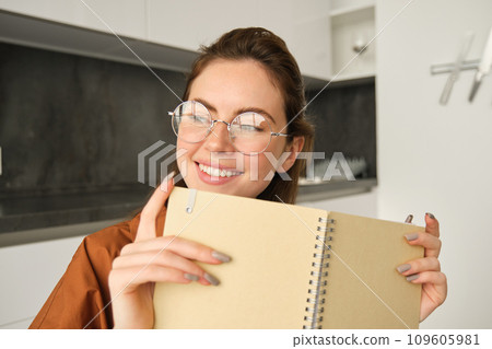 Portrait of cute smiling woman reading her notes, holding notebook 109605981