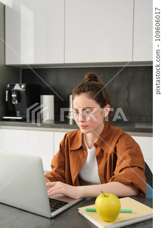 Vertical shot of woman working from home, business owner using laptop, browsing social media on computer, wearing glasses Vertical shot of woman working from home, business owner using laptop, browsing social media on computer, wearing glasses 109606017
