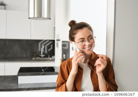 Portrait of happy woman at home, answers phone call, talking on mobile, holding smartphone and smiling 109606167