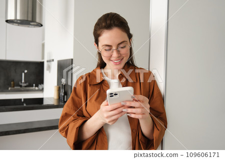 Beautiful woman checking social media while using smartphone at home. Smiling young female using mobile phone app and playing game, shopping online or reading news. Copy space 109606171