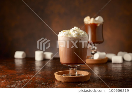 Hot chocolate with whipped cream in a glass mug on a old brown table. 109606219