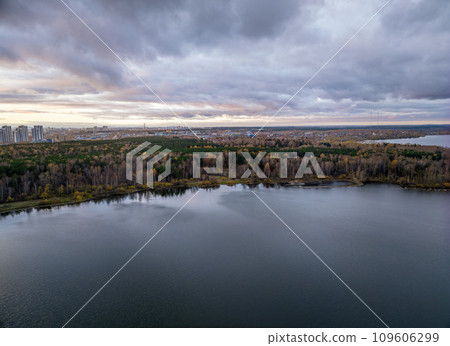 Autumn forest on lake shore at sunset and city on horizon, aerial view Autumn forest on lake shore at sunset and city on horizon, aerial view 109606299