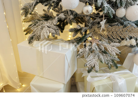Christmas gift boxes in golden and white wrapping paper of Santa presents under Xmas tree decorated with garland lights, festive balls or baubles, ornaments. Traditional New Year holidays celebration Christmas gift boxes in golden and white wrapping paper of Santa presents under Xmas tree decorated with garland lights, festive balls or baubles, ornaments. Traditional New Year holidays celebration 109607074