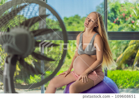 A pregnant woman seeks relief from an abnormal heatwave by using a fan, ensuring her comfort and well-being during sweltering conditions 109608651