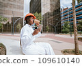 Young ethnic woman using smartphone while drinking coffee on street 109610140