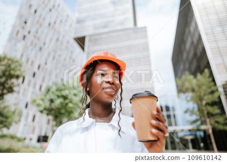 Happy black woman in helmet standing with coffee cup in daylight 109610142