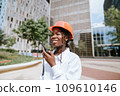 Happy black woman in helmet standing and speaking on walkie talkie in daylight 109610146