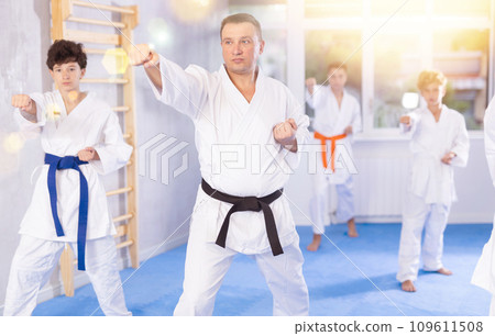 Karate kids in kimono performing kata moves with their teacher in foreground in gym during group training Karate kids in kimono performing kata moves with their teacher in foreground in gym during group training 109611508