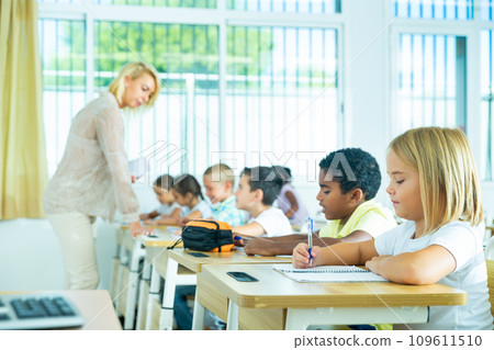 Diligent tweens studying in classroom with female teacher 109611510