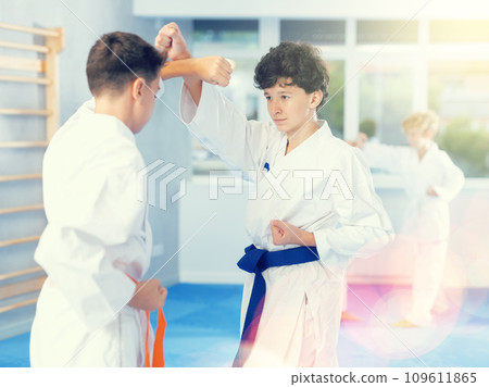 Teenagers in kimonos working on hand strikes in pairs during group training Teenagers in kimonos working on hand strikes in pairs during group training 109611865