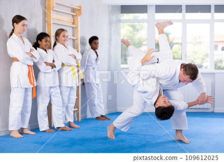 Judo coach shows fighting techniques in sparring with a boy for group of young athletes Judo coach shows fighting techniques in sparring with a boy for group of young athletes 109612025