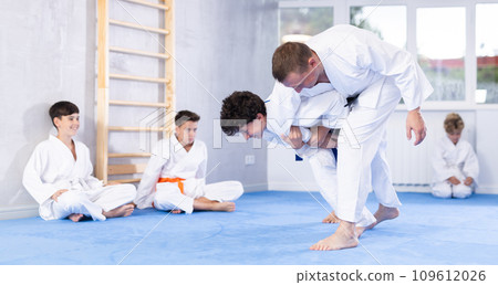 Skilled judo trainer demonstrating wrestling technique on juvenile practitioner Skilled judo trainer demonstrating wrestling technique on juvenile practitioner 109612026