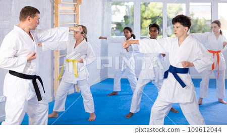 Tween boy in kimono practicing punches as part of kata during group training Tween boy in kimono practicing punches as part of kata during group training 109612044