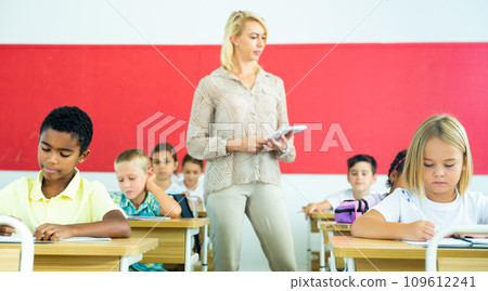 Focused preteen pupils studying in classroom with female teacher 109612241