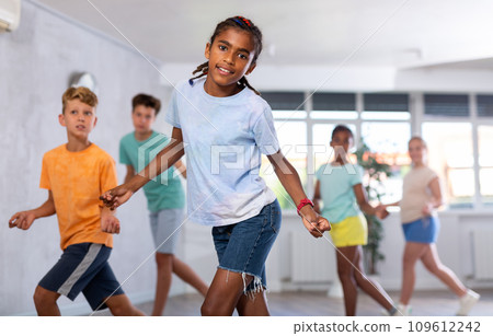 Positive juvenile boy engaged in Rock 'n' Roll dance in training room with children's group 109612242