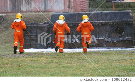 Firefighter Rescue team training in fire fighting extinguisher. Firefighter teamwork fighting with flame using fire hose chemical water foam spray engine. Fireman wear hard hat, safety suit uniform 109612482