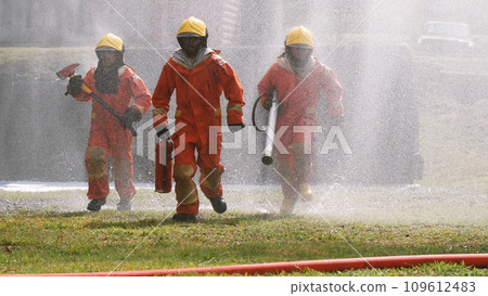 Firefighter Rescue team training in fire fighting extinguisher. Firefighter teamwork fighting with flame using fire hose chemical water foam spray engine. Fireman wear hard hat, safety suit uniform 109612483