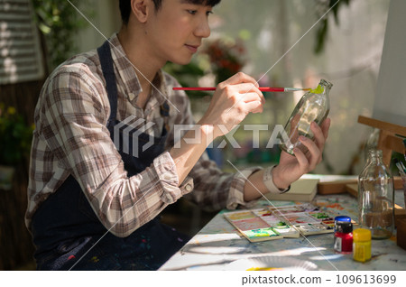 A positive and handsome young Asian man is handcrafting a decorative bottle in his home garden. 109613699