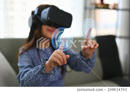 Little girl wearing VR headset and touching virtual button interacting with digital interface Little girl wearing VR headset and touching virtual button interacting with digital interface 109614743