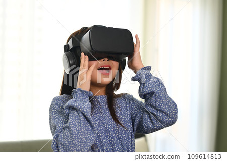 Excited little girl playing games, experiencing via VR headset. Innovative technologies concept Excited little girl playing games, experiencing via VR headset. Innovative technologies concept 109614813