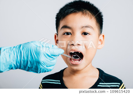 Pediatric dentist examines a child's mouth after removal of a loose milk tooth. Dental assistant assists in examination with dental instruments. Doctor uses mouth mirror to checking teeth cavity Pediatric dentist examines a child's mouth after removal of a loose milk tooth. Dental assistant assists in examination with dental instruments. Doctor uses mouth mirror to checking teeth cavity 109615420
