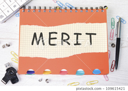 Merit word is written on a sheet in a cage lying on a notebook on the table next to stationery Merit word is written on a sheet in a cage lying on a notebook on the table next to stationery 109615421