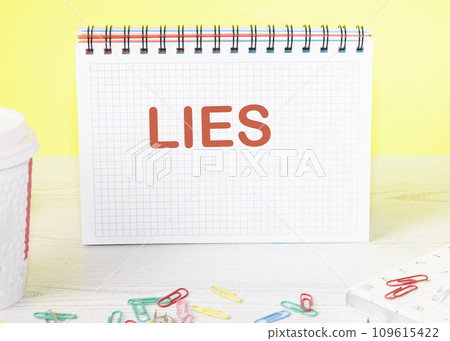 Lies the word is written on a blank sheet in a notebook standing on a table on a yellow background Lies the word is written on a blank sheet in a notebook standing on a table on a yellow background 109615422