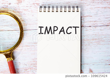 IMPACT a word written on a notebook on wooden boards next to a magnifying glass IMPACT a word written on a notebook on wooden boards next to a magnifying glass 109615424