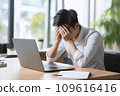 A man officer in a white shirt at an office desk holds his head, possibly suffering from a migraine or office syndrome 109616416