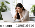 A woman officer at an office desk holds her head, possibly suffering from a migraine or office syndrome 109616419