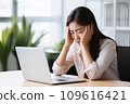 A woman officer at an office desk holds her head, possibly suffering from a migraine or office syndrome 109616421