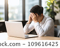 A man officer in a white shirt at an office desk holds his head, possibly suffering from a migraine or office syndrome 109616425