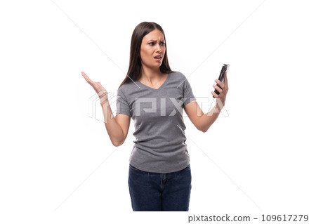 surprised brunette leader woman dressed in a gray t-shirt looks at the smartphone screen on a white surprised brunette leader woman dressed in a gray t-shirt looks at the smartphone screen on a white 109617279
