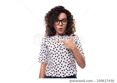 portrait of a young curly brunette well-groomed slender lady dressed in polka dot blouse in black 109617436