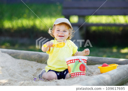 Cute toddler girl playing in sand on outdoor playground. Beautiful baby having fun on sunny warm summer sunny day. Happy healthy child with sand toys and in colorful fashion clothes. Cute toddler girl playing in sand on outdoor playground. Beautiful baby having fun on sunny warm summer sunny day. Happy healthy child with sand toys and in colorful fashion clothes. 109617695