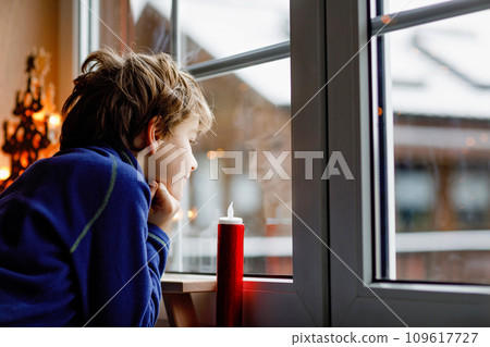 Happy adorable kid boy sitting near window and looking outside on snow on Christmas day or morning. Smiling healthy child fascinated observing snowfall and big snowflakes 109617727