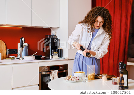 Woman adding pepper into blender with chickpeas while making hummus 109617801