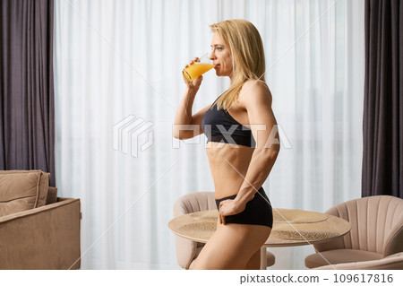 Bodybuilder woman drinks juice after workout at home Bodybuilder woman drinks juice after workout at home 109617816