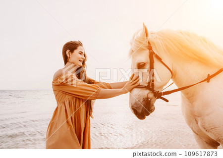 A white horse and a woman in a dress stand on a beach, with the A white horse and a woman in a dress stand on a beach, with the 109617873
